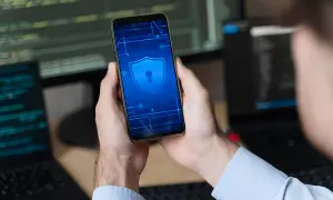 Ręce trzymają smartfon z ikoną tarczy i klucza, symbolizującą bezpieczeństwo. To wskazówka, jak odblokować telefon bez utraty danych.