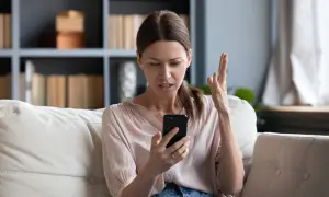 Zirytowana kobieta sprawdza telefon, który nie ma internetu.