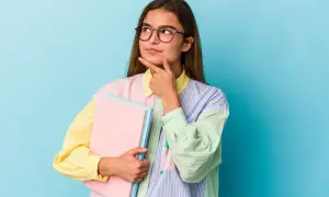 Młoda kobieta w okularach z książkami zastanawia się nad ciekawymi kierunkami studiów dla niezdecydowanych.