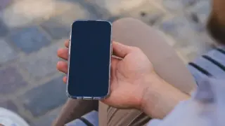 Mężczyzna trzyma iPhone'a w przezroczystym etui. Zastanawia się, jak wyłączyć iPhone'a, aby zrobić sobie przerwę od technologii.