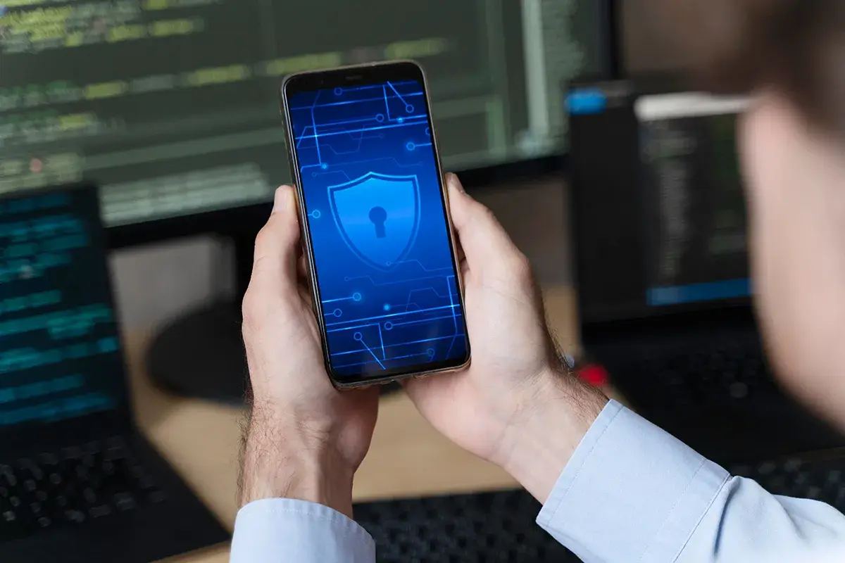Ręce trzymają smartfon z ikoną tarczy i klucza, symbolizującą bezpieczeństwo. To wskazówka, jak odblokować telefon bez utraty danych.