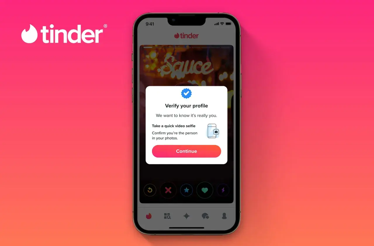 Na ekranie telefonu widoczny jest portal randkowy Tinder. Użytkownik jest proszony o weryfikację profilu za pomocą selfie wideo.