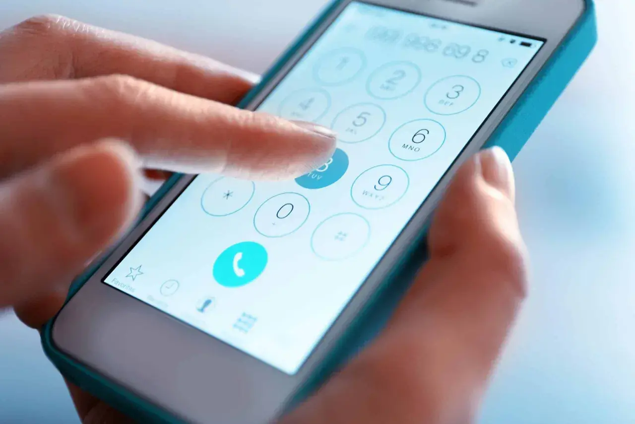 Dłoń wybiera numer na ekranie smartfona. Sprawdź numer telefonu, zanim zadzwonisz.