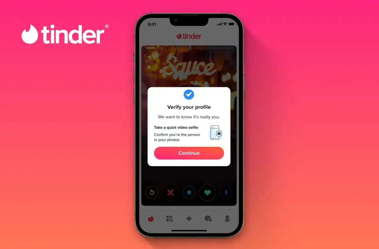 Na ekranie telefonu widoczny jest portal randkowy Tinder. Użytkownik jest proszony o weryfikację profilu za pomocą selfie wideo.