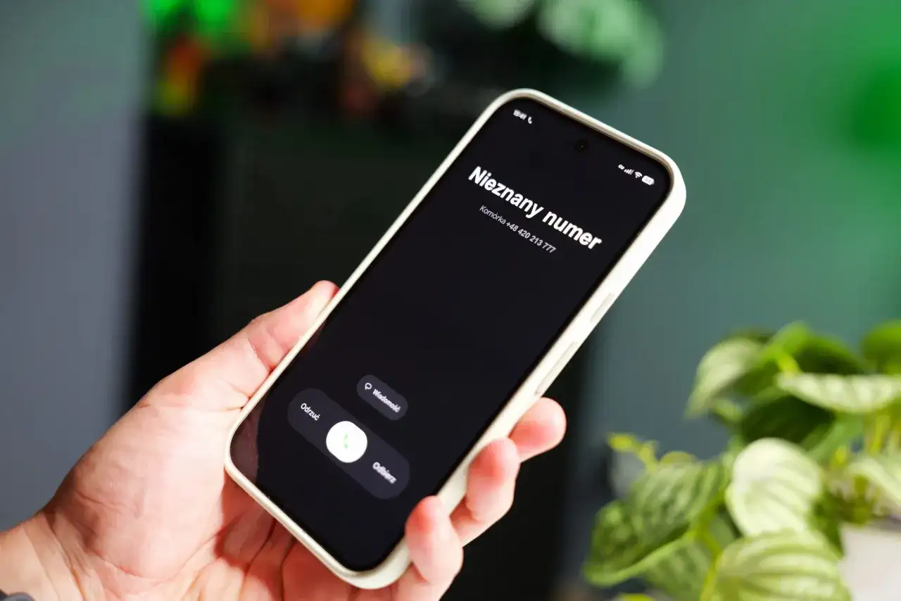 Dłoń trzyma smartfon z ekranem blokady, na którym widnieje komunikat "Nieznany numer" i numer telefonu. Warto sprawdzić numer telefonu, zanim się go odbierze.