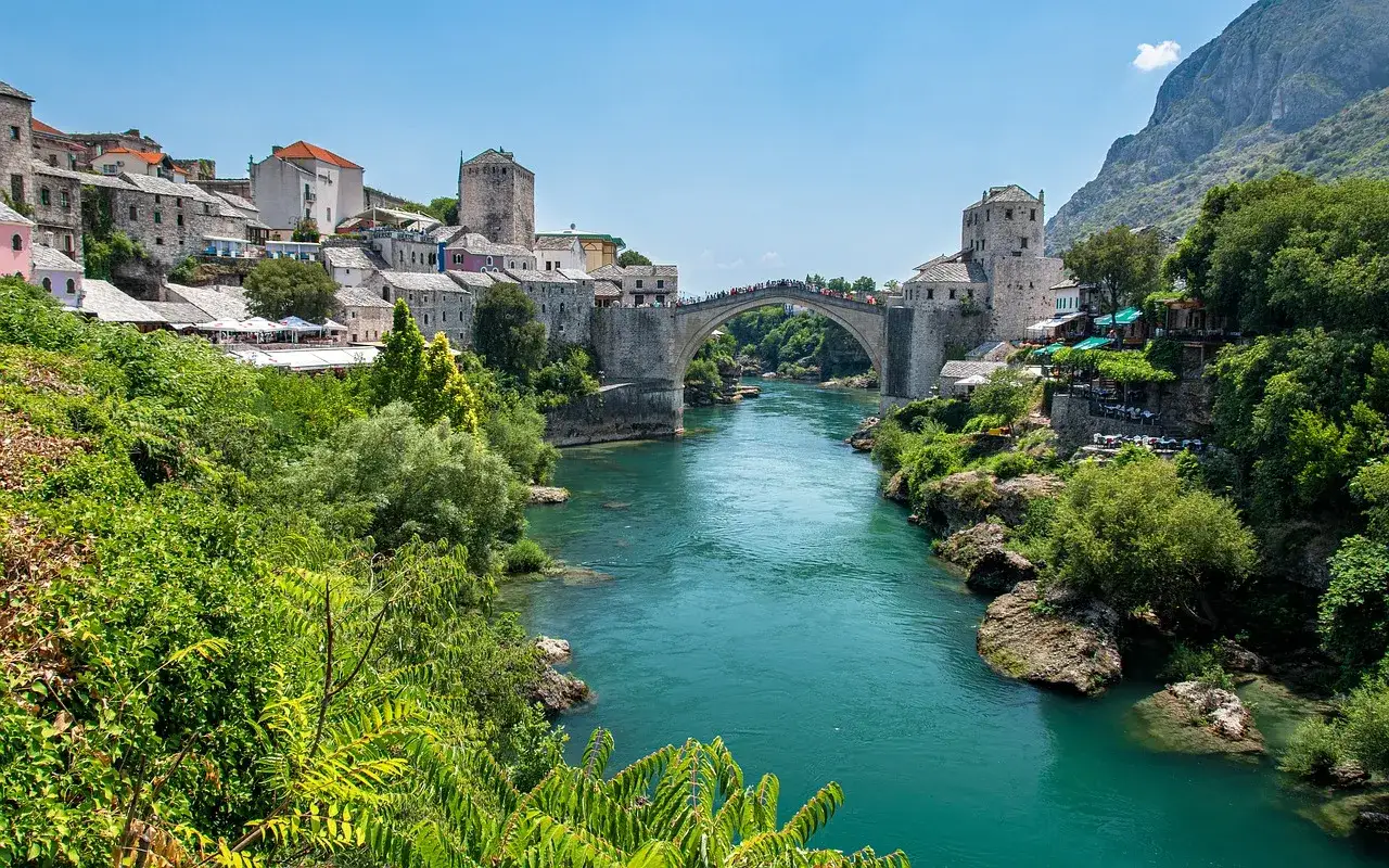Mostar, Bośnia i Hercegowina. Stary Most nad turkusową rzeką Neretwą, otoczony kamiennymi budynkami i bujną zielenią.