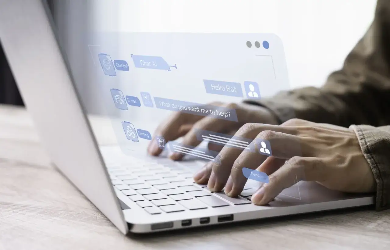 Ręce piszą na laptopie, interfejs chatbota z pytaniem 