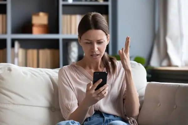 Zirytowana kobieta sprawdza telefon, który nie ma internetu.