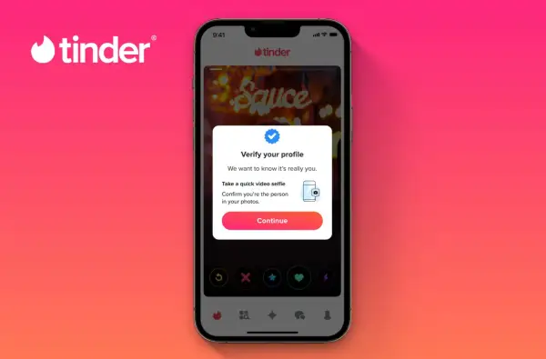 Na ekranie telefonu widoczny jest portal randkowy Tinder. Użytkownik jest proszony o weryfikację profilu za pomocą selfie wideo.