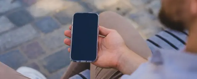 Mężczyzna trzyma iPhone'a w przezroczystym etui. Zastanawia się, jak wyłączyć iPhone'a, aby zrobić sobie przerwę od technologii.